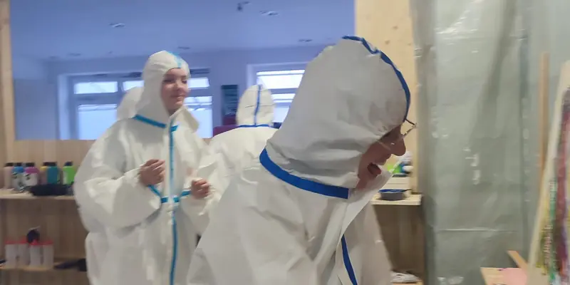 Zwei Personen ziehen im Atelier die weißen Maleranzüge an