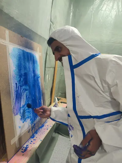 Mann trägt mit dem Pinsel kräftiges Blau auf die Leinwand auf
