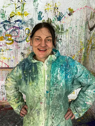 Olga Lautenschläger im farbverschmierten Anzug vor der Handabdruck-Wand