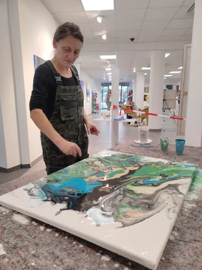 Olga verteilt die gegossene Farbe auf der liegenden Leinwand